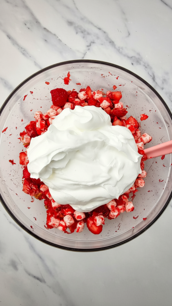 cool whipped cream being added to the mixture for Strawberry Fluff Salad