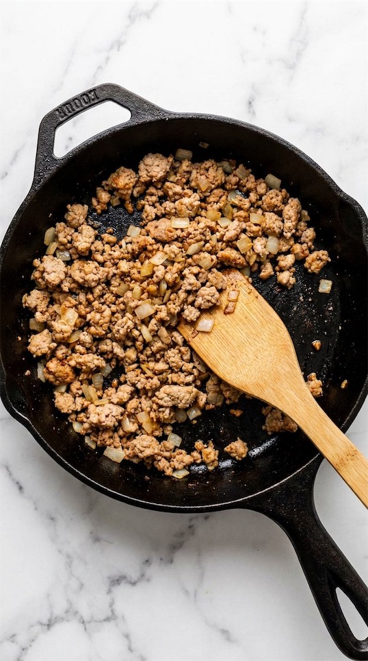 turkey mince and onions being cooked in black skillet 